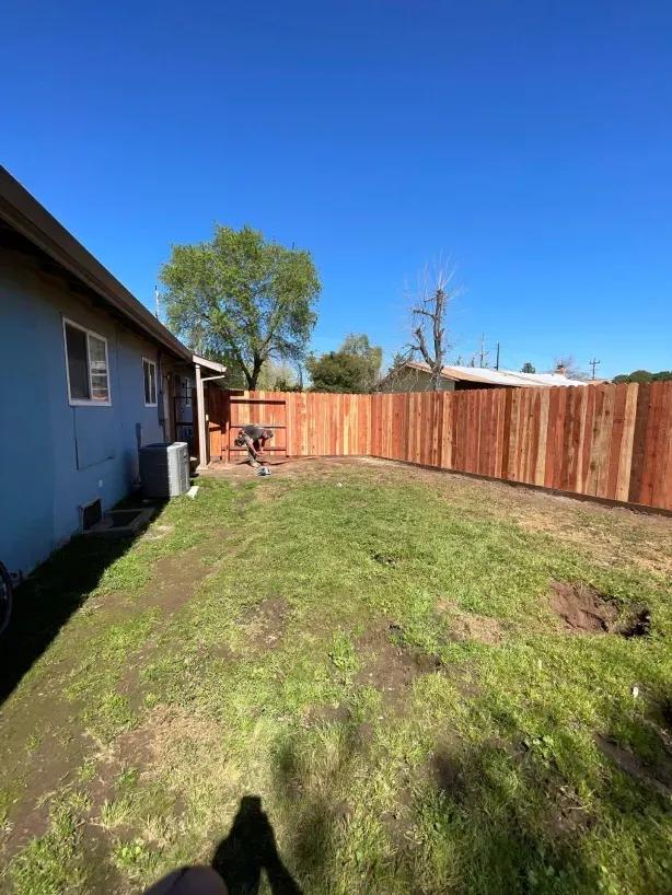 A backyard with a wooden fence and a house in the background.