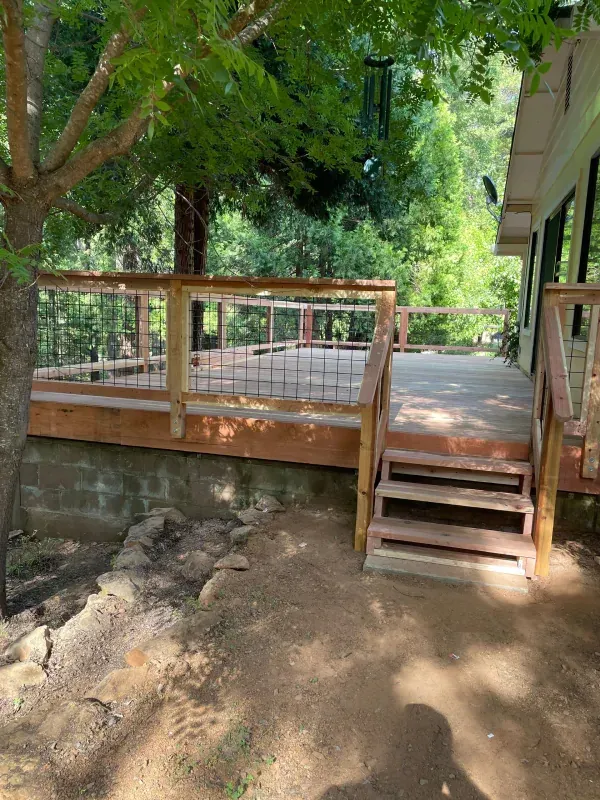 A wooden deck with stairs leading up to it is surrounded by trees.