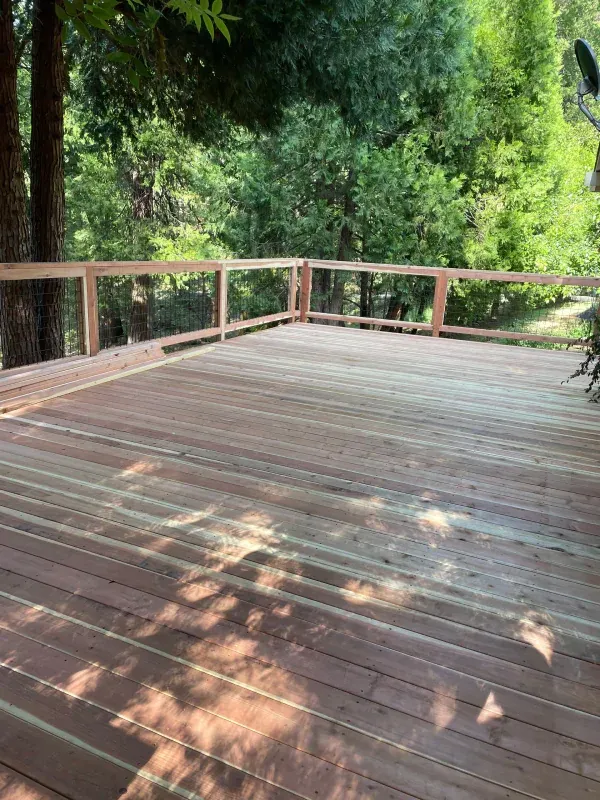 A wooden deck with a railing and trees in the background.