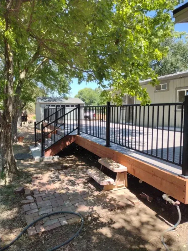 A wooden deck with stairs and a metal railing in front of a house.