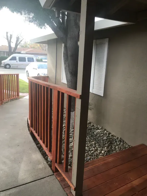 A porch with a wooden railing and a tree in the background