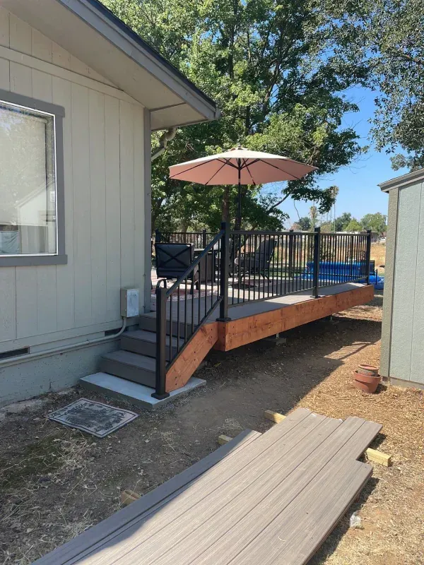 A deck with a pink umbrella is being built in front of a house.