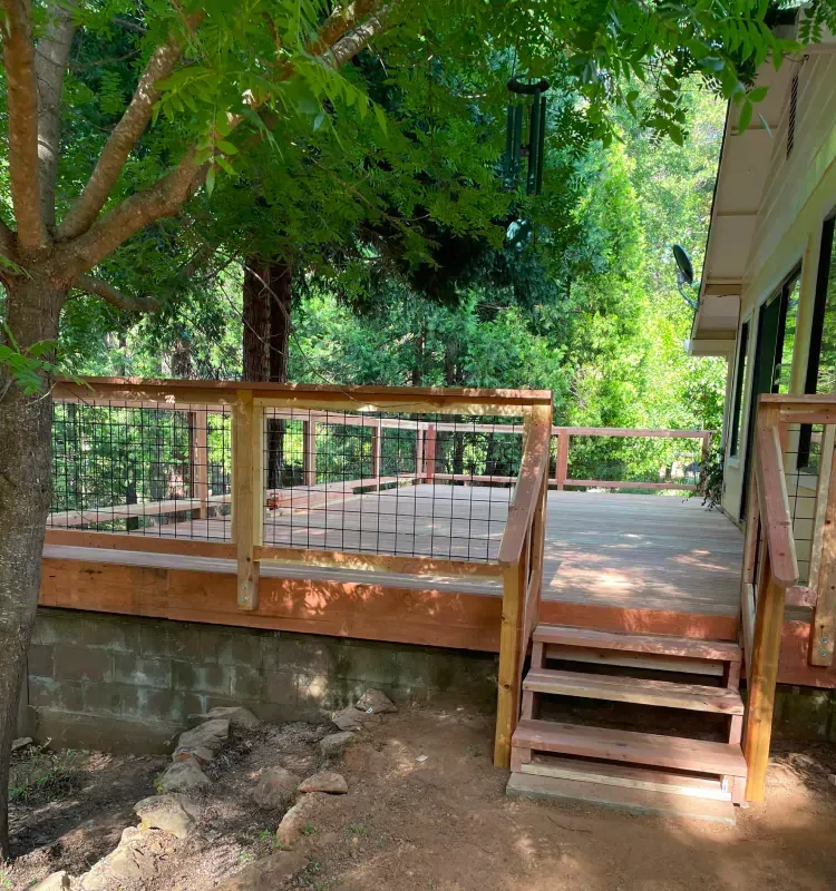 A wooden deck with stairs leading up to it is surrounded by trees.