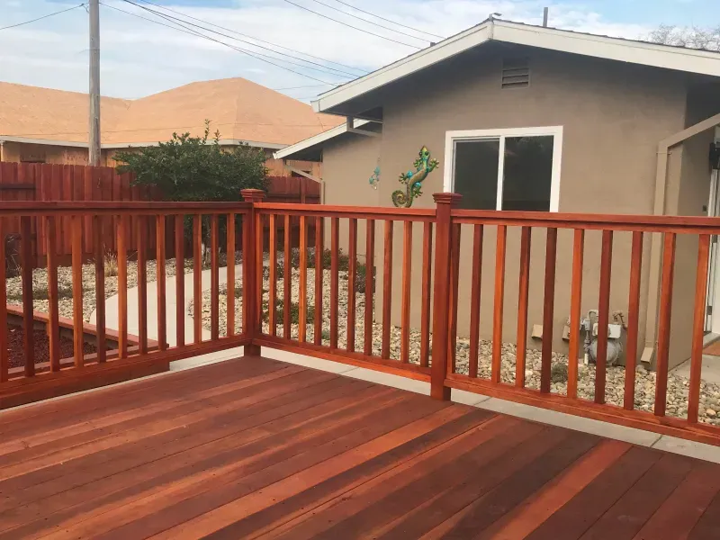 A wooden deck with a wooden railing in front of a house.