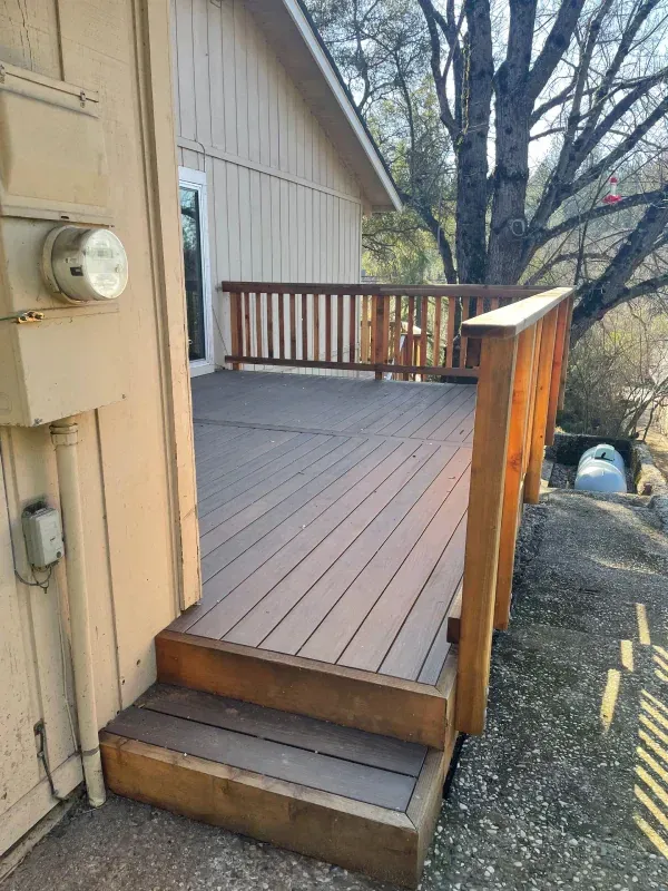 A wooden deck with stairs leading up to it is next to a house.