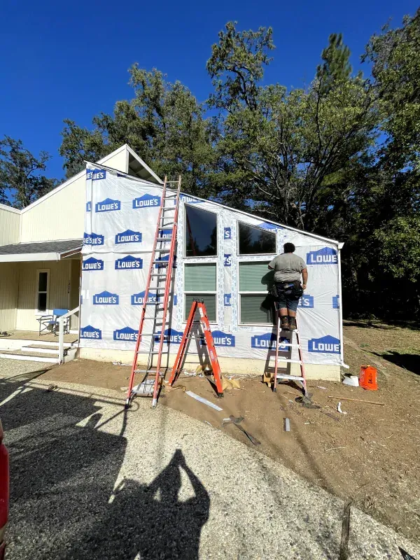 A man is standing on a ladder in front of a house.