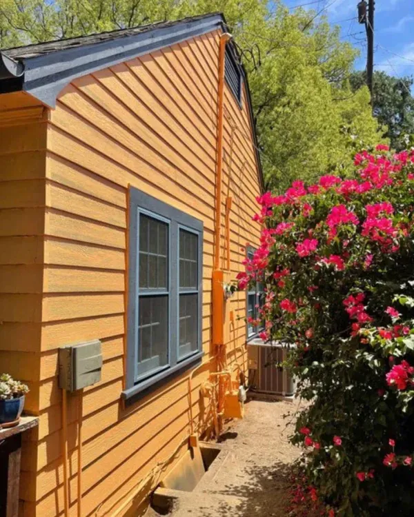 A house with orange siding and blue windows is surrounded by pink flowers