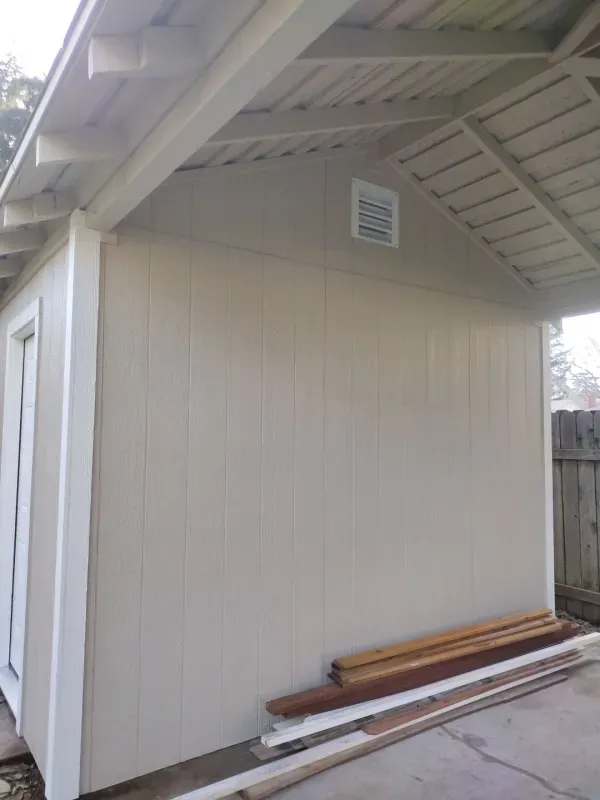 A white shed with a roof and a wooden bench in front of it.