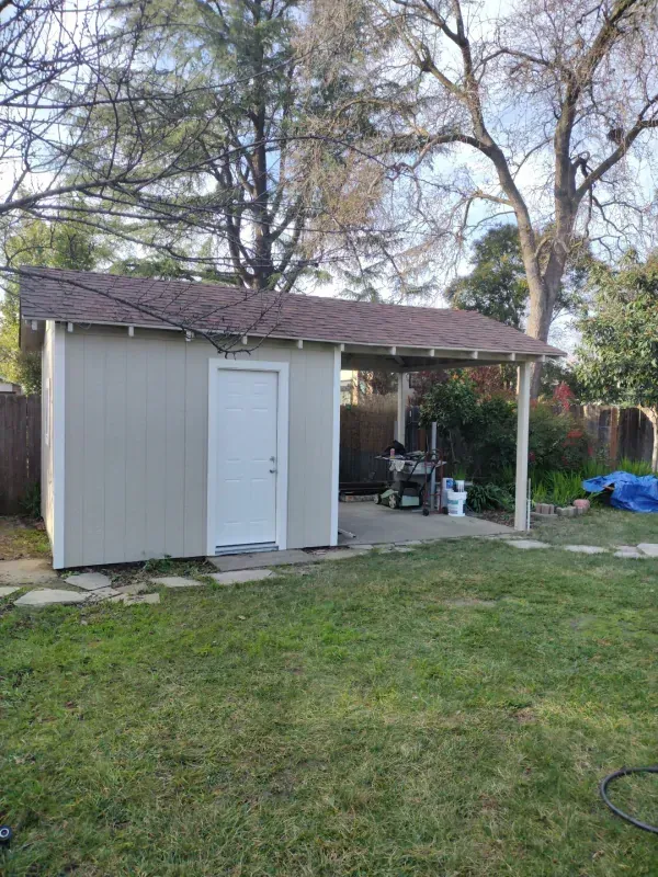 A shed with a porch in the backyard of a house.