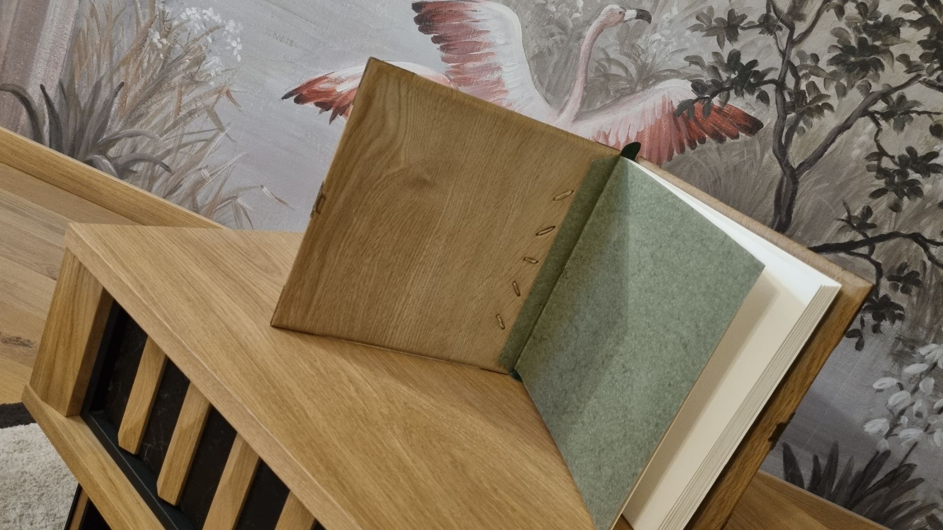 Un livre est posé sur une étagère en bois devant un tableau représentant un flamant rose.