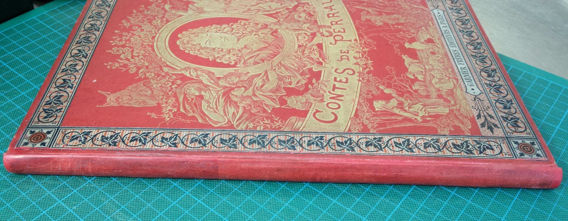 Un livre rouge avec une bordure dorée est posé sur une table bleue.