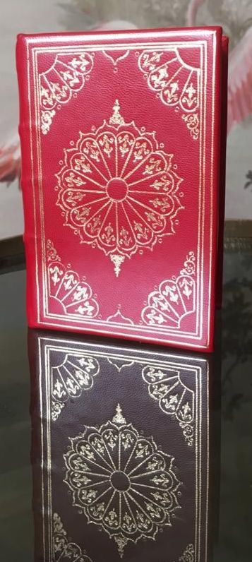 Un livre rouge avec un motif doré sur la couverture est posé sur une table.