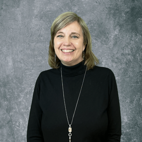 Smiling woman in a black turtleneck and long necklace against a gray backdrop