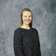 Smiling person in a dark sweater against a gray studio backdrop
