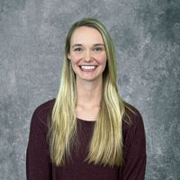 Smiling woman with long blonde hair in a burgundy top against a gray backdrop