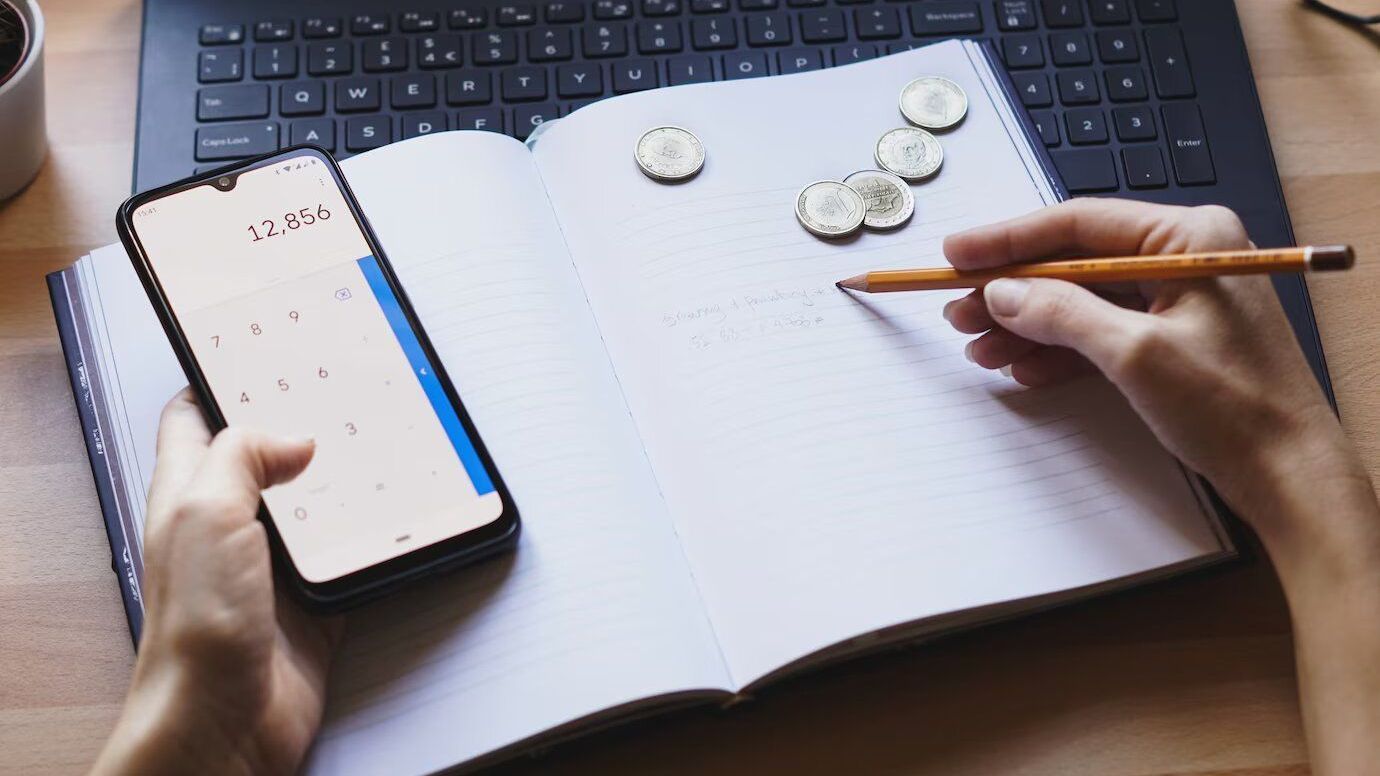 Una persona sostiene un teléfono celular y escribe en un cuaderno.