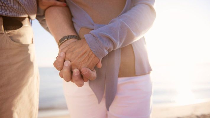 Ein Mann und eine Frau halten am Strand Händchen.