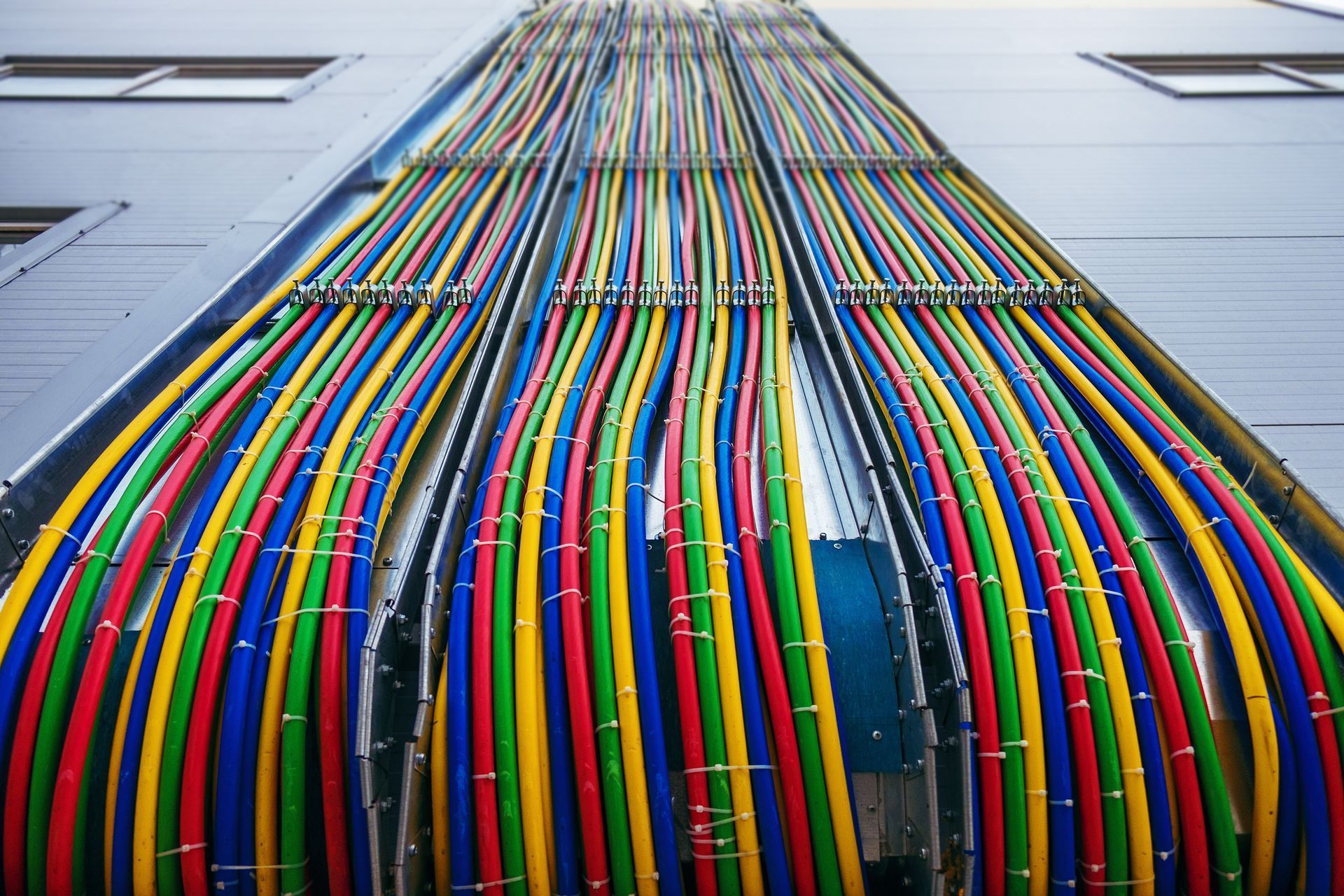 Many brightly colored cables run in organized vertical lines along the exterior wall of a building.