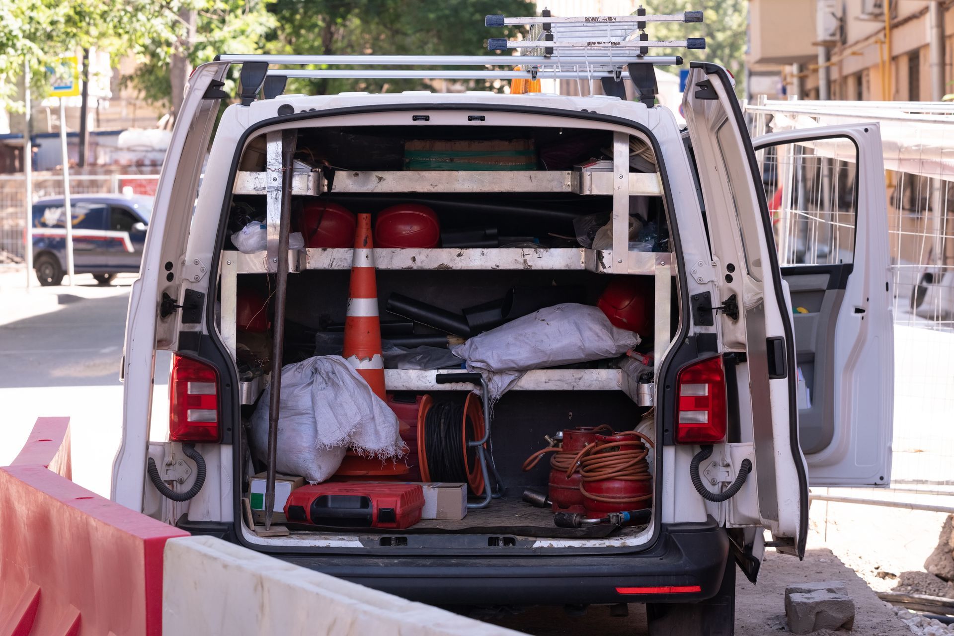 Open back doors of a white service van revealing shelves stocked with equipment, a traffic cone, and construction gear.