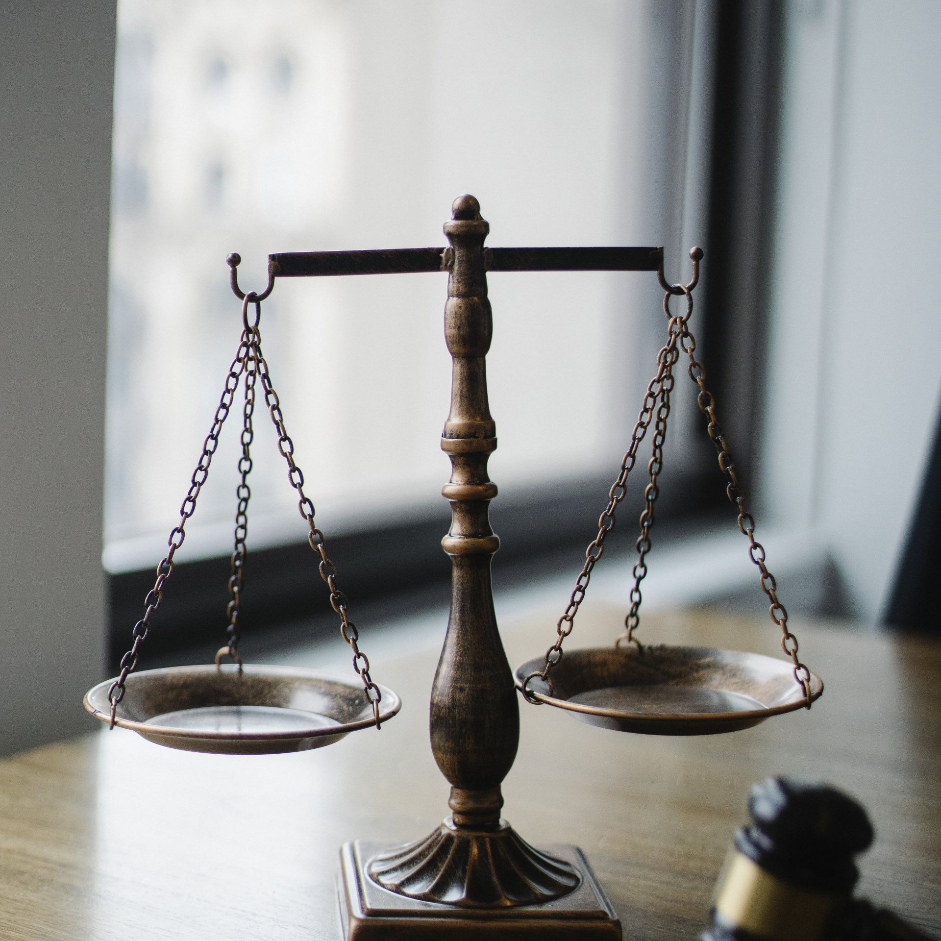 A scale of justice sits on a wooden table next to a gavel