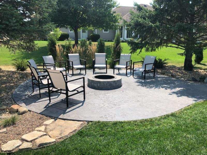 A fire pit in the middle of a patio with chairs around it.