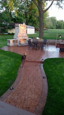 A walkway leading to a patio with a fireplace and a table and chairs.