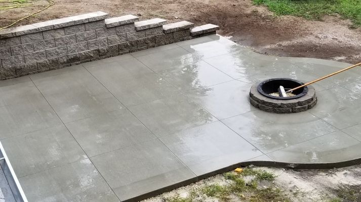 A concrete patio with a fire pit in the middle of it.