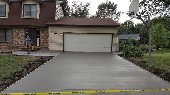 A man is walking down a concrete driveway in front of a house.