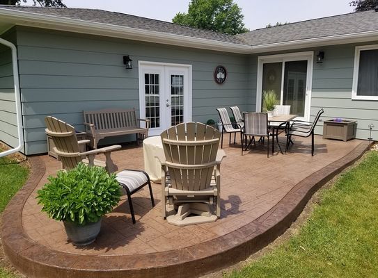 A patio with chairs , a table and a fire pit in front of a house.