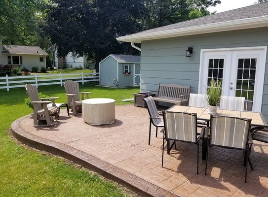 A patio with a table and chairs and a fire pit in front of a house.