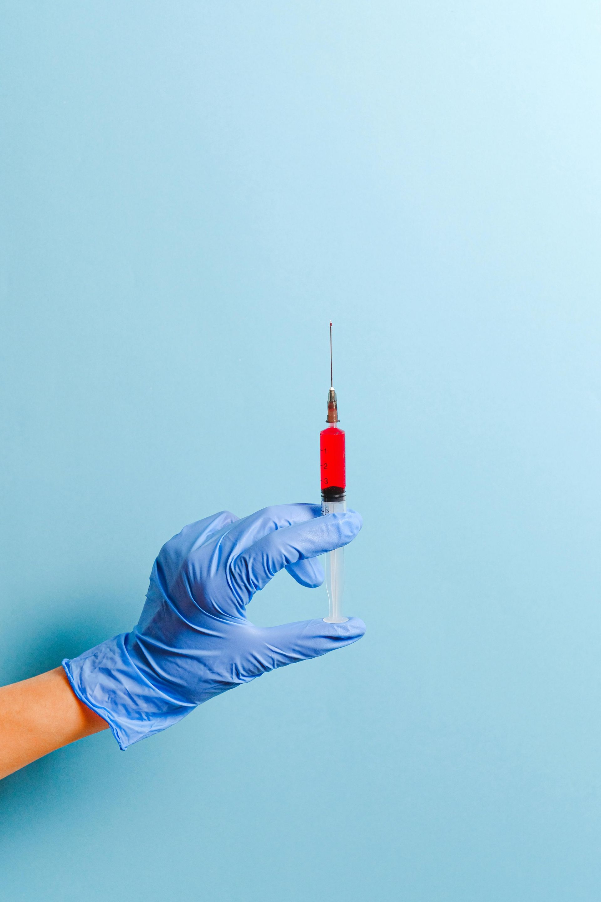 A hand in a blue glove is holding a syringe on a blue background.