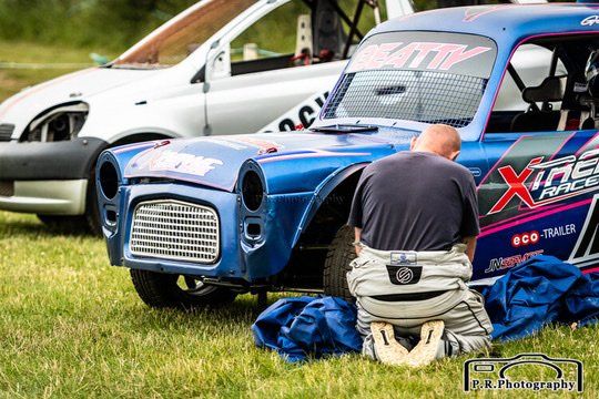 A man is kneeling down in front of a blue race car.