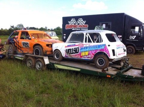 Two race cars are on a trailer in a field.