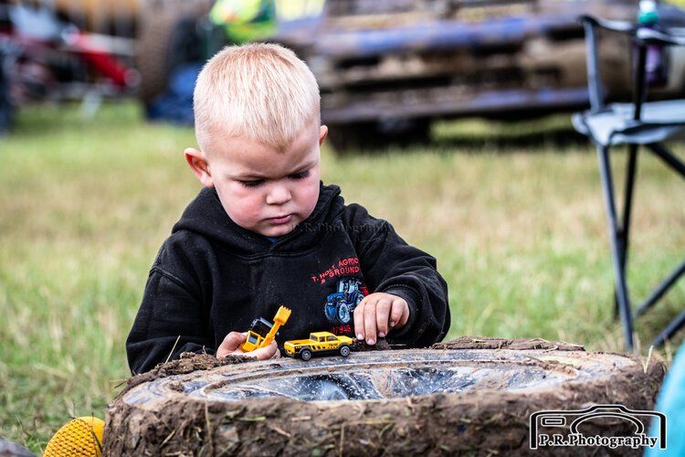 A little boy is playing with a toy car on a log.