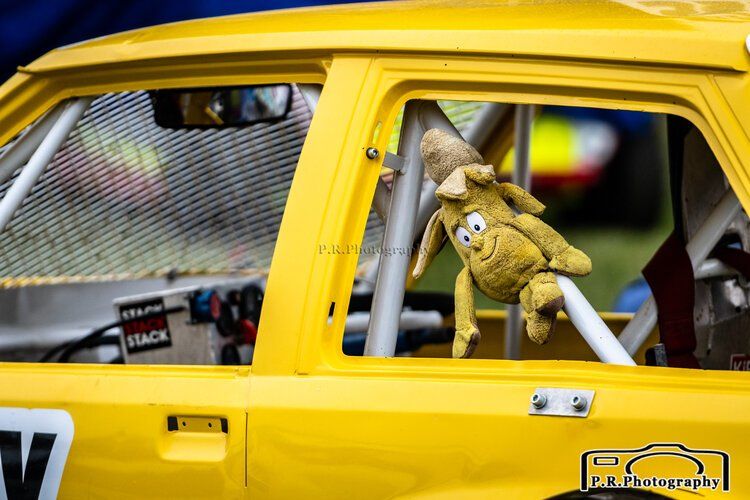 A stuffed animal is sticking out of the window of a yellow race car.