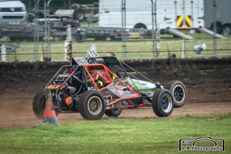 A dune buggy is driving down a dirt track.