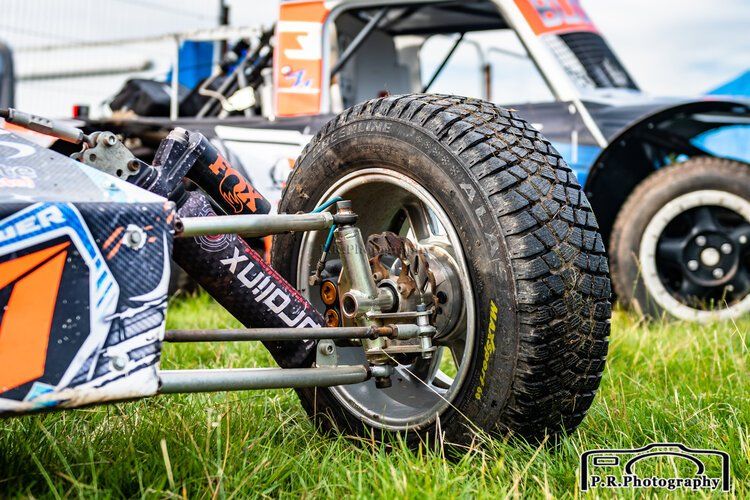 A race car is parked in a grassy field next to another race car.