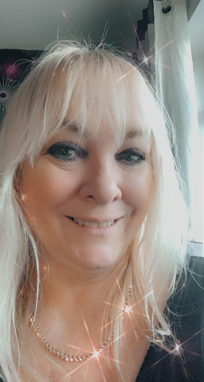 A woman with blonde hair and a necklace is smiling for the camera.