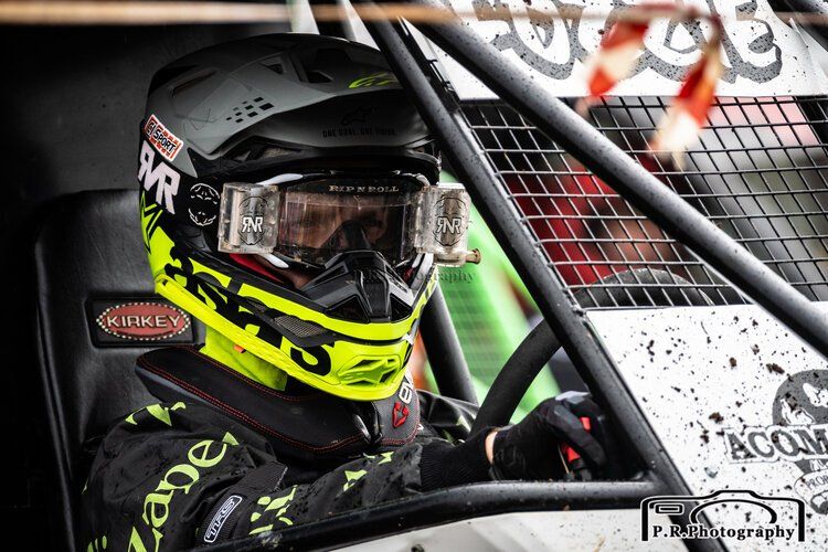 A man wearing a helmet and goggles is sitting in a race car.