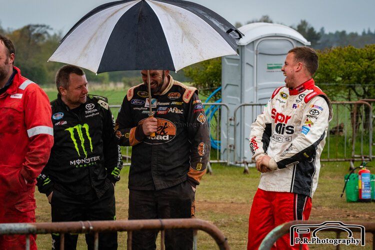 A man is standing next to a race car in a field.