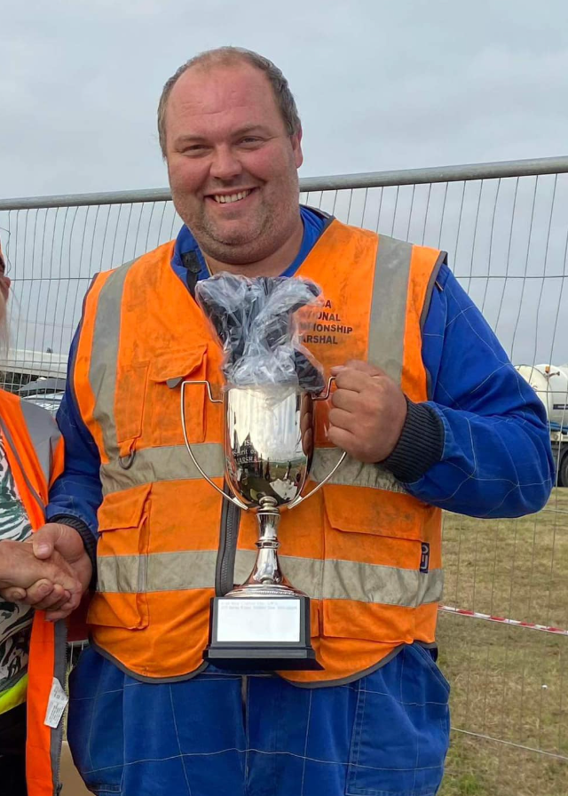 A man in an orange vest is holding a trophy