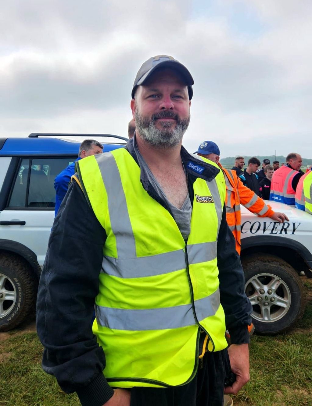 A man wearing a yellow vest is standing in front of a recovery vehicle