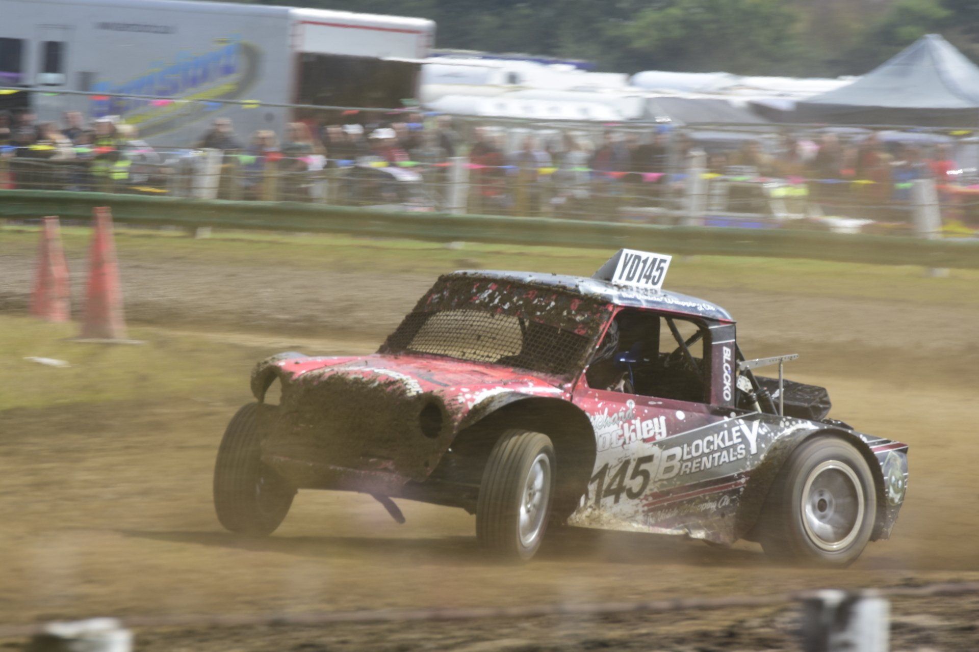 A red race car is driving on a dirt track.