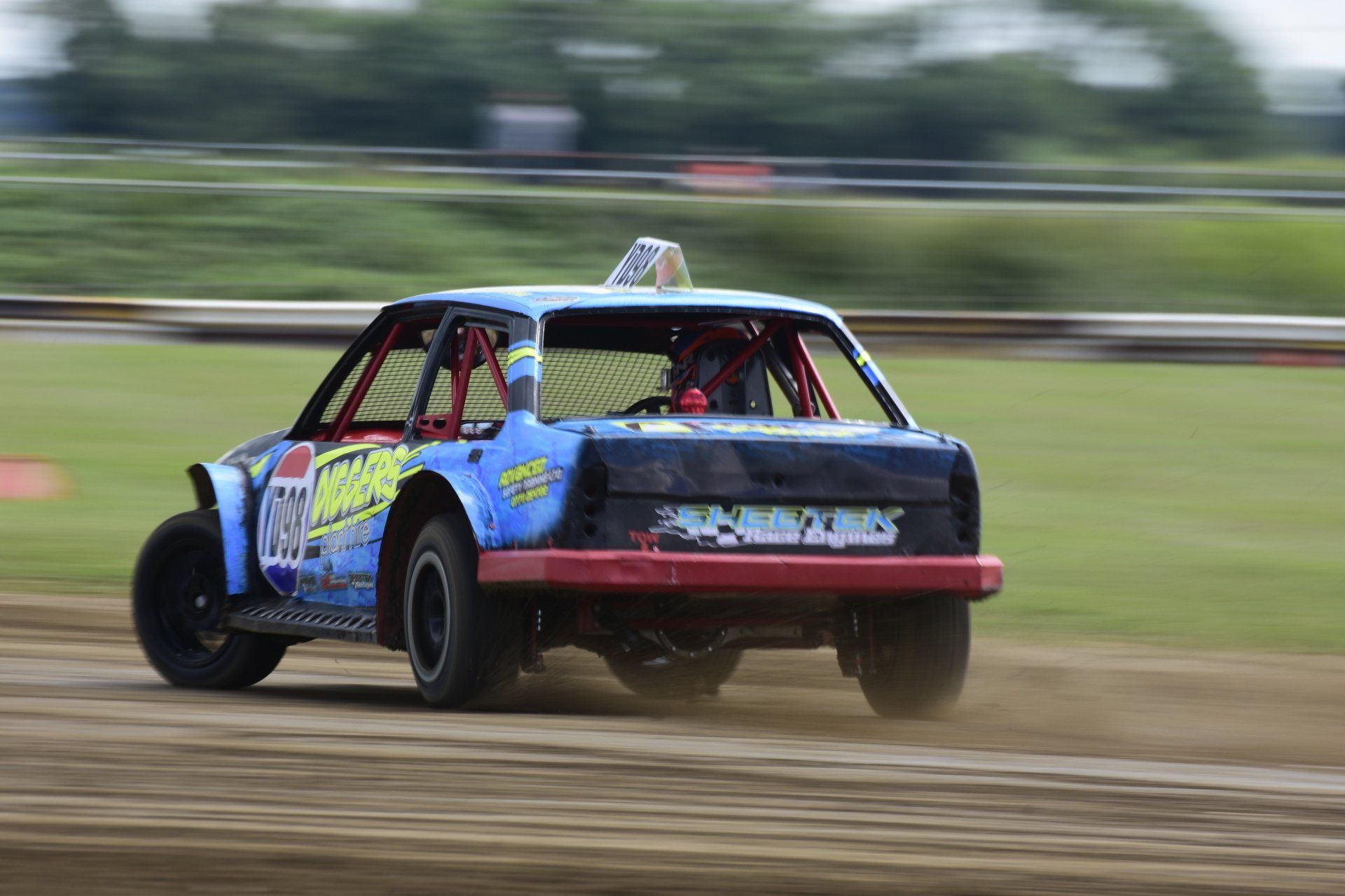 A blue and red race car is driving down a dirt road.