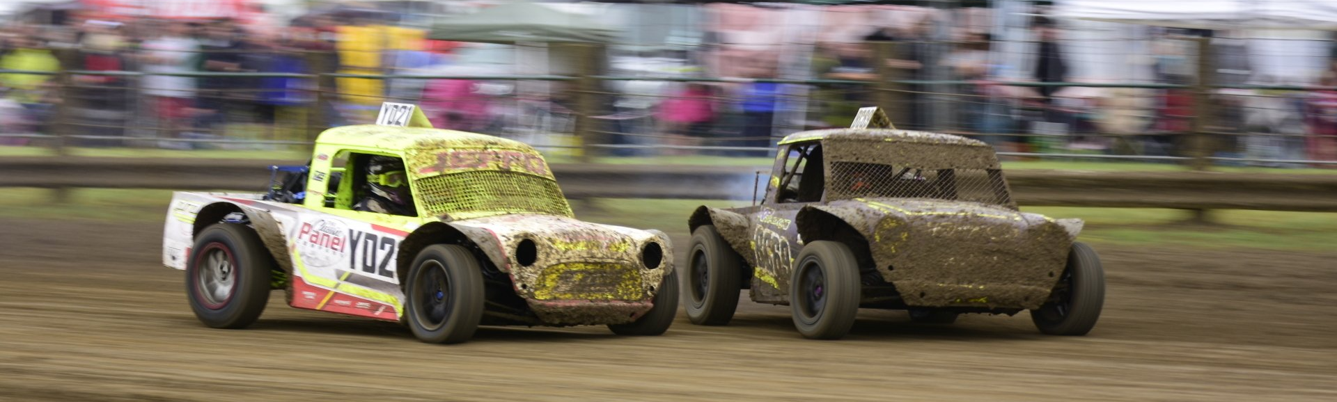 Two dirt trucks are racing on a dirt track.