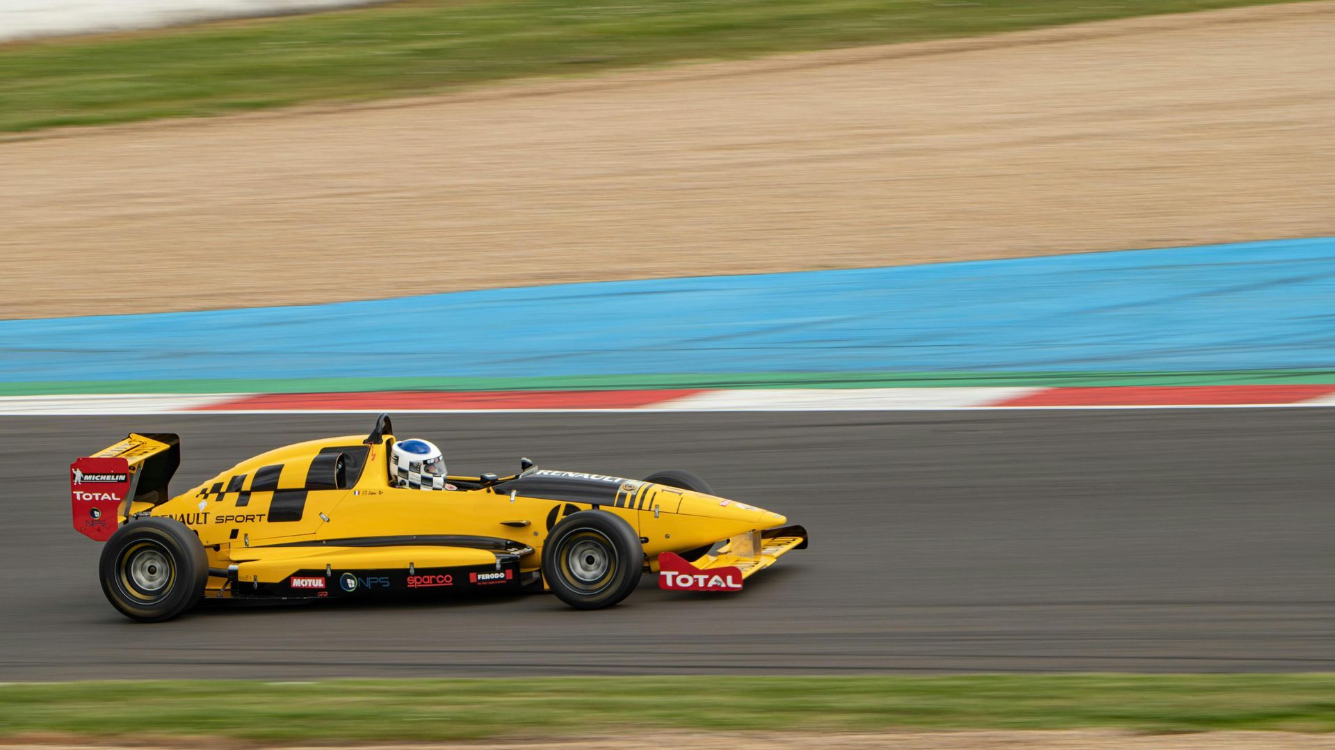 A yellow race car is driving down a race track.