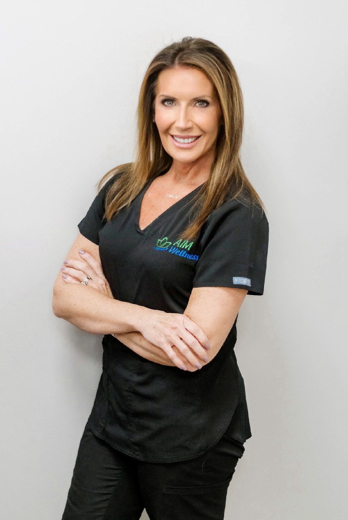 Woman in black medical scrubs standing with arms crossed and smiling against a light gray background