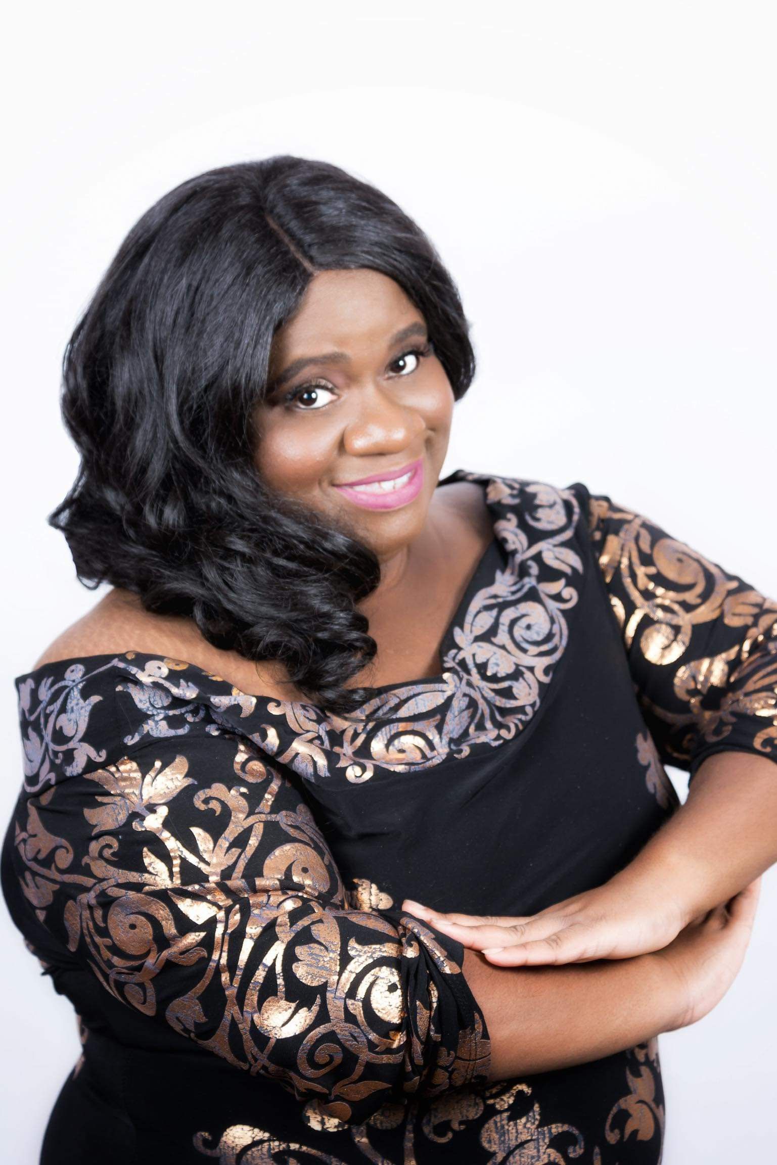 A woman in a black and gold dress is standing with her arms crossed.