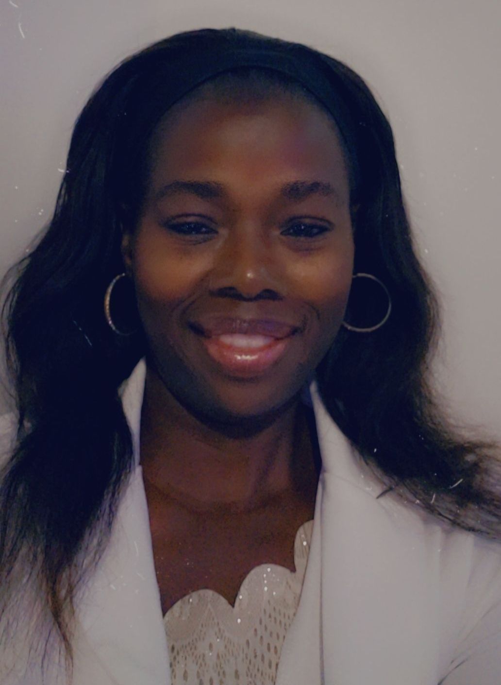 A woman wearing a white coat and hoop earrings is smiling for the camera.