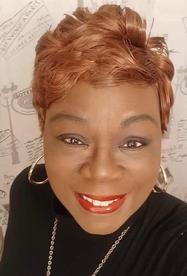 A woman with short red hair and red lipstick is smiling for the camera.